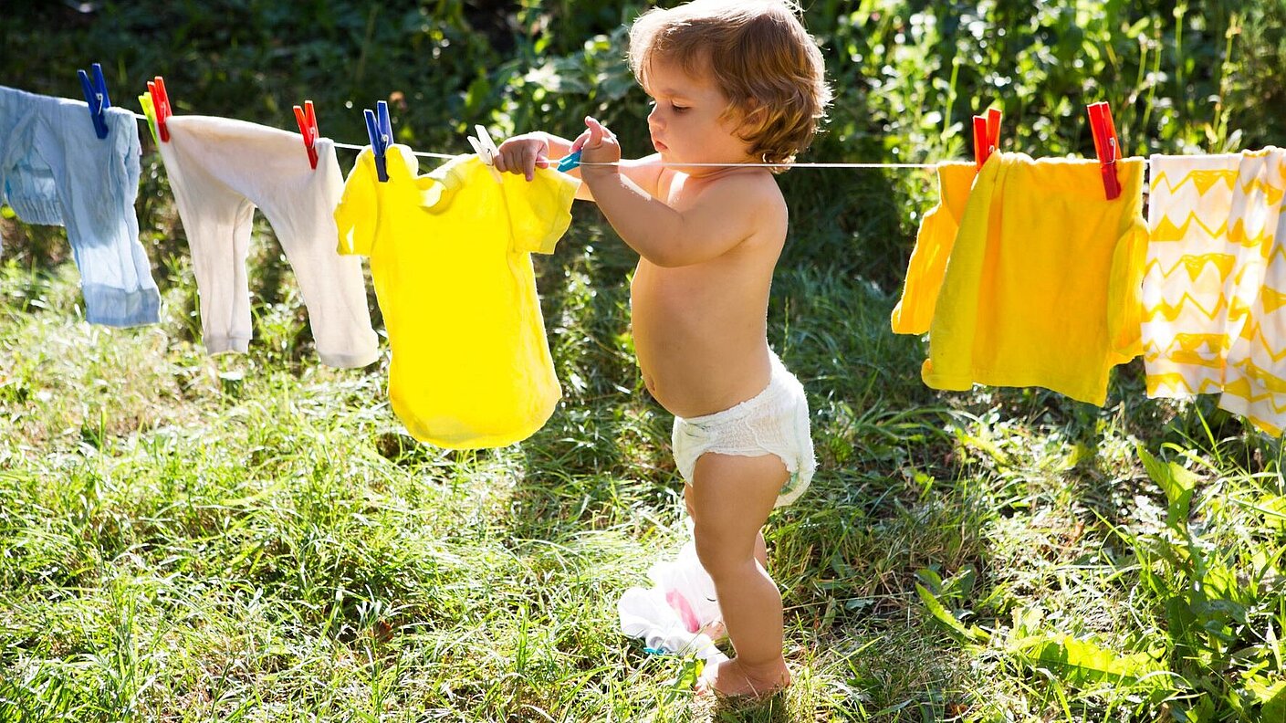 Kleines Kind hängt an einem sonnigen Tag kleidung draußen auf