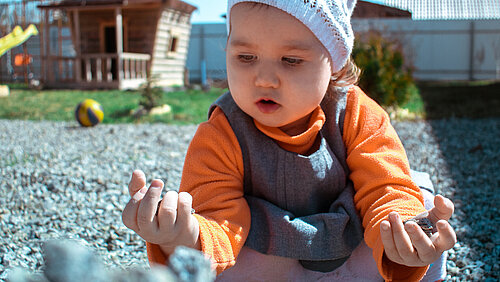 Ein Baby spielt mit Kieselsteinen vor einem Spielplatz
