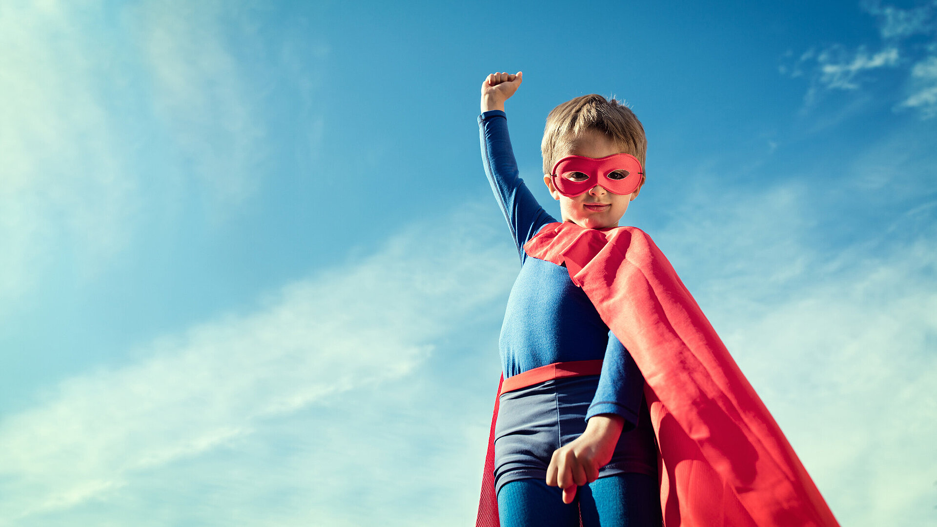 Kleiner Junge verkleidet als Superheld mit rotem Umhang und Maske