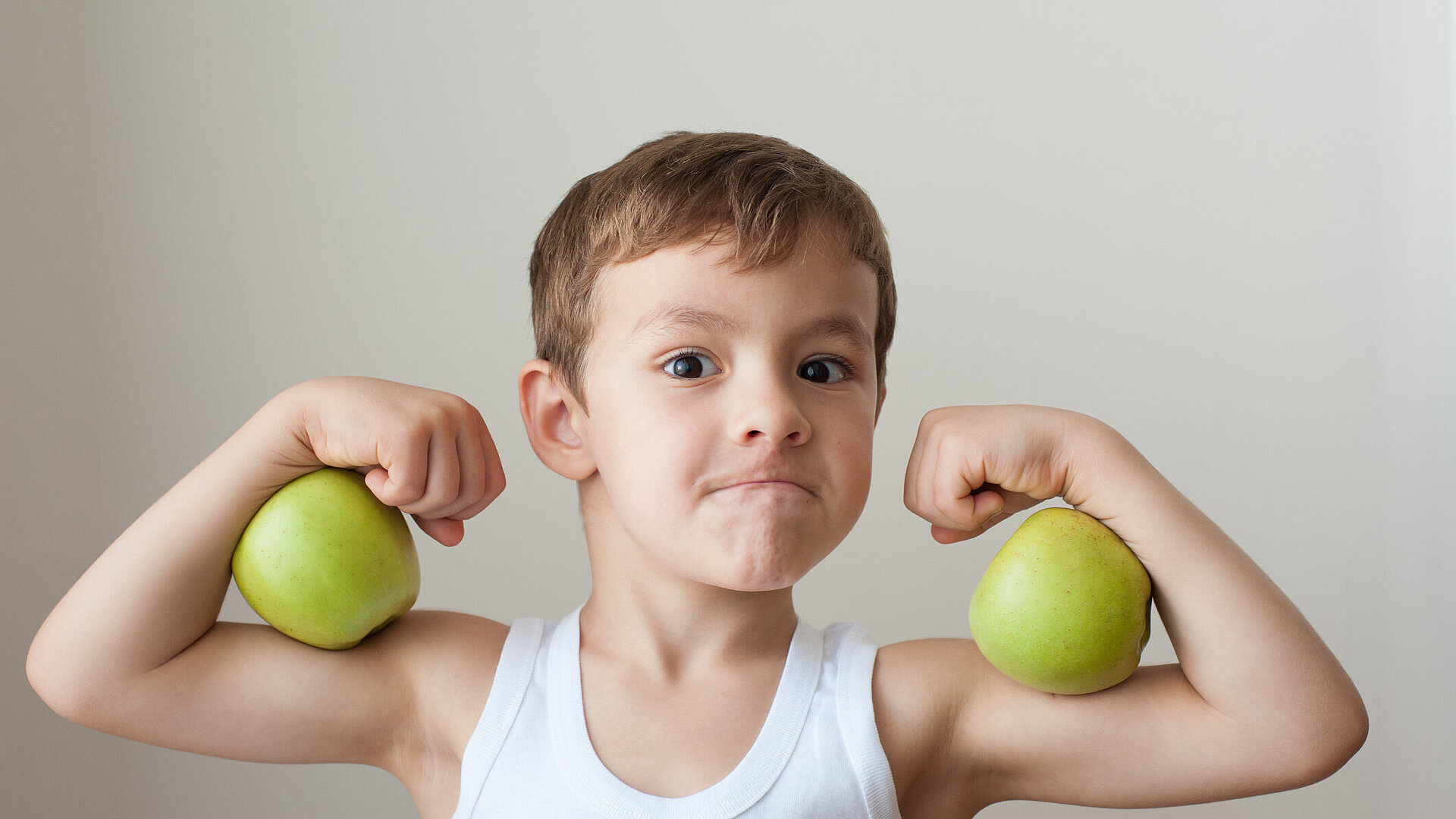 Kind spannt Armmuskeln an und hält zwei äpfel zwischen den Armen