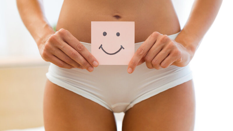 Eine Frau hält einen Post-IT Zettel mit einem Smiley for den Bauch