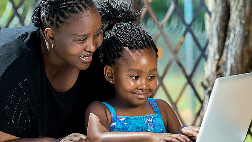 Afrikanische Mutter und Kind schauen auf einen laptop im Freien
