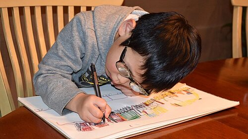 Kleiner Junge zeichnet auf einem Blatt Papier