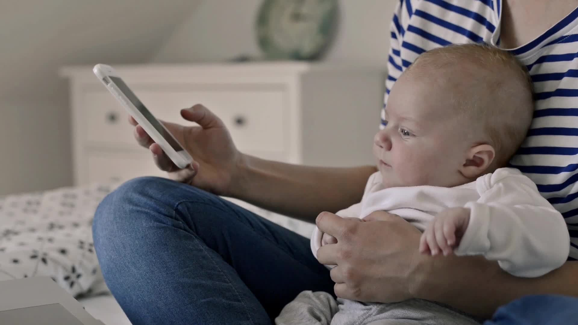 Mutter mit Baby Sohn sitzen auf dem Bett und schauen auf ein Handy 