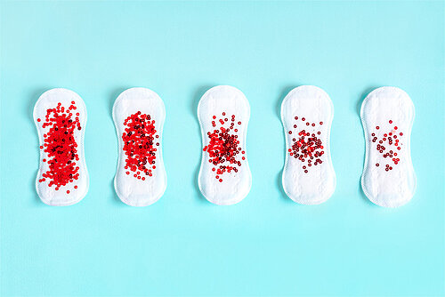 Fünf Binden mit roten Pailletten zeigen typischen Menstruationsverlauf
