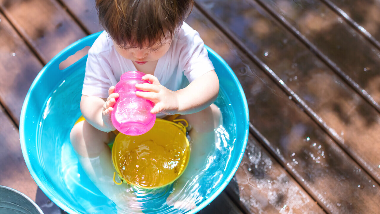 Baby sitzt in einem Becken mit Wasser und spielt
