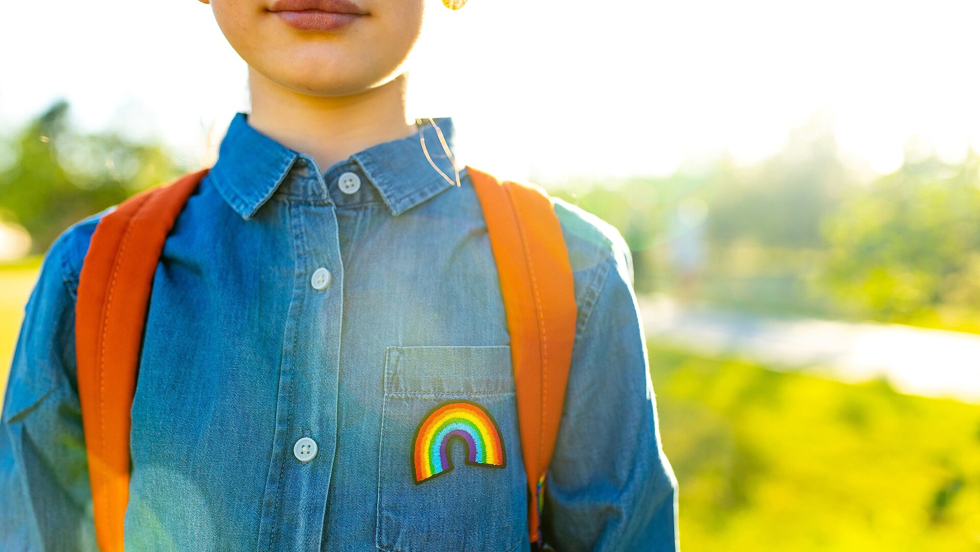 Kind mit Rucksack, Jeansjacke und einem Regenbogenanstecker