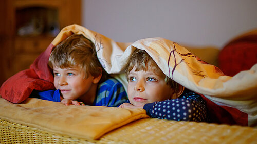Zwei Jungen liegen unter der Decke und schauen Fernseh 