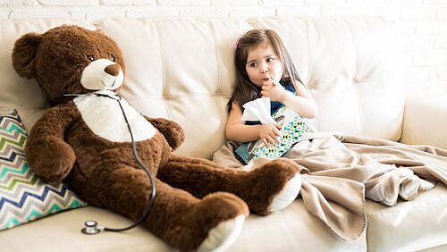 Kind sitzt mit einem großen Teddybär auf dem Sofa