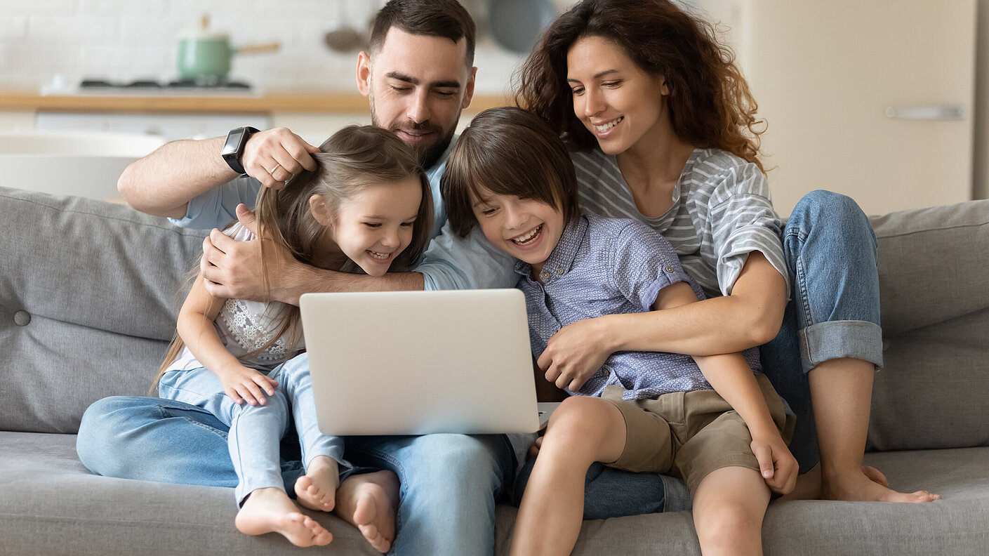 Familie von vier Personen sitzen zusammen am Laptop und lachen