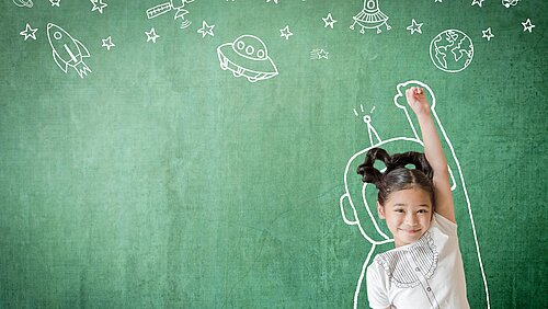 Ein Kind steht vor einer Tafel auf der mit Kreise Raumschiffe und Sterne gemalt sind