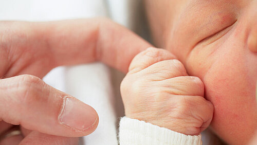 Baby hält mittels Greifreflex den Finger eines Erwachsenen