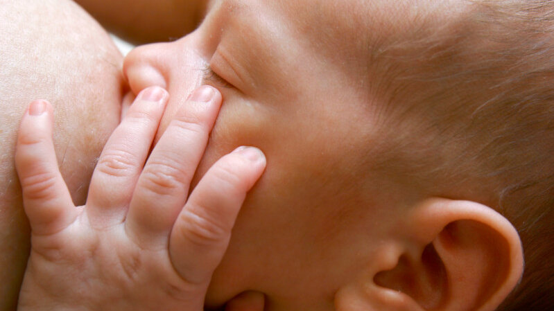 Baby saugt an der Brust und hält Hand an das Gesicht