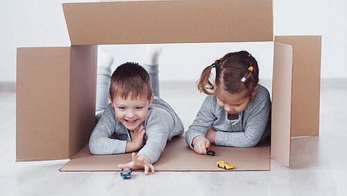 Bruder und Schwester spielen in Pappkartons im Kindergarten