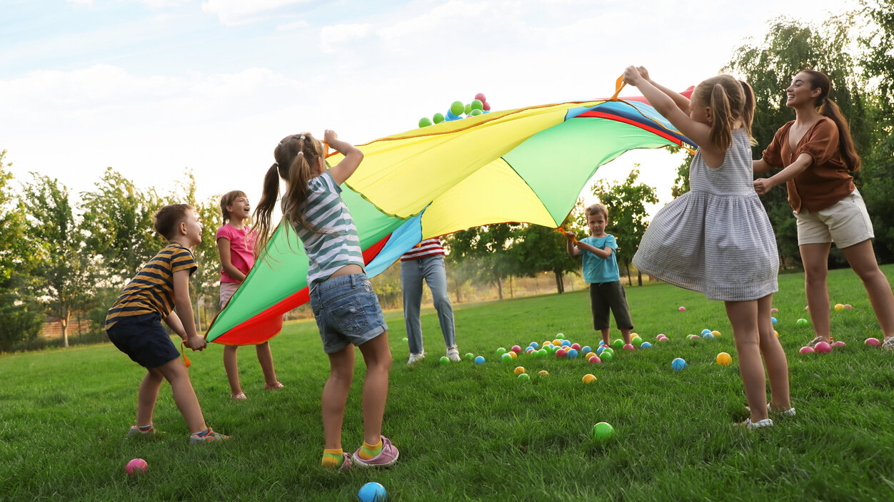 Kinder spielen auf einer Wiese mit einem bunten Fallschirm
