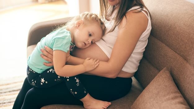 Kind sitzt auf dem Schoß einer schwangeren Frau und legt sein Kopf an den Bauch