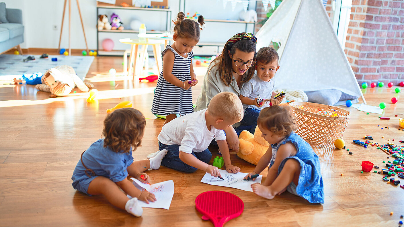 Lehrerin und kleinkind Gruppe sitzen mit Papier und Buntstiften auf dem Boden