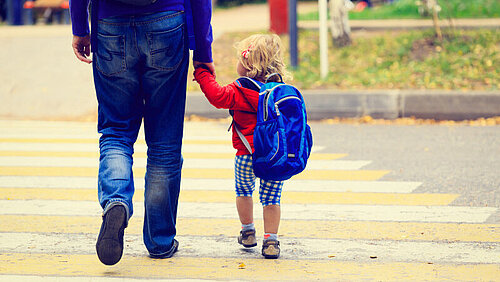 Ein Kind mit Rucksack hält die Hand eines Erwachsenen