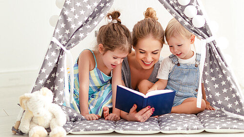 Eine Frau liest zwei Kindern eine Geschichte in einem Zelt vor