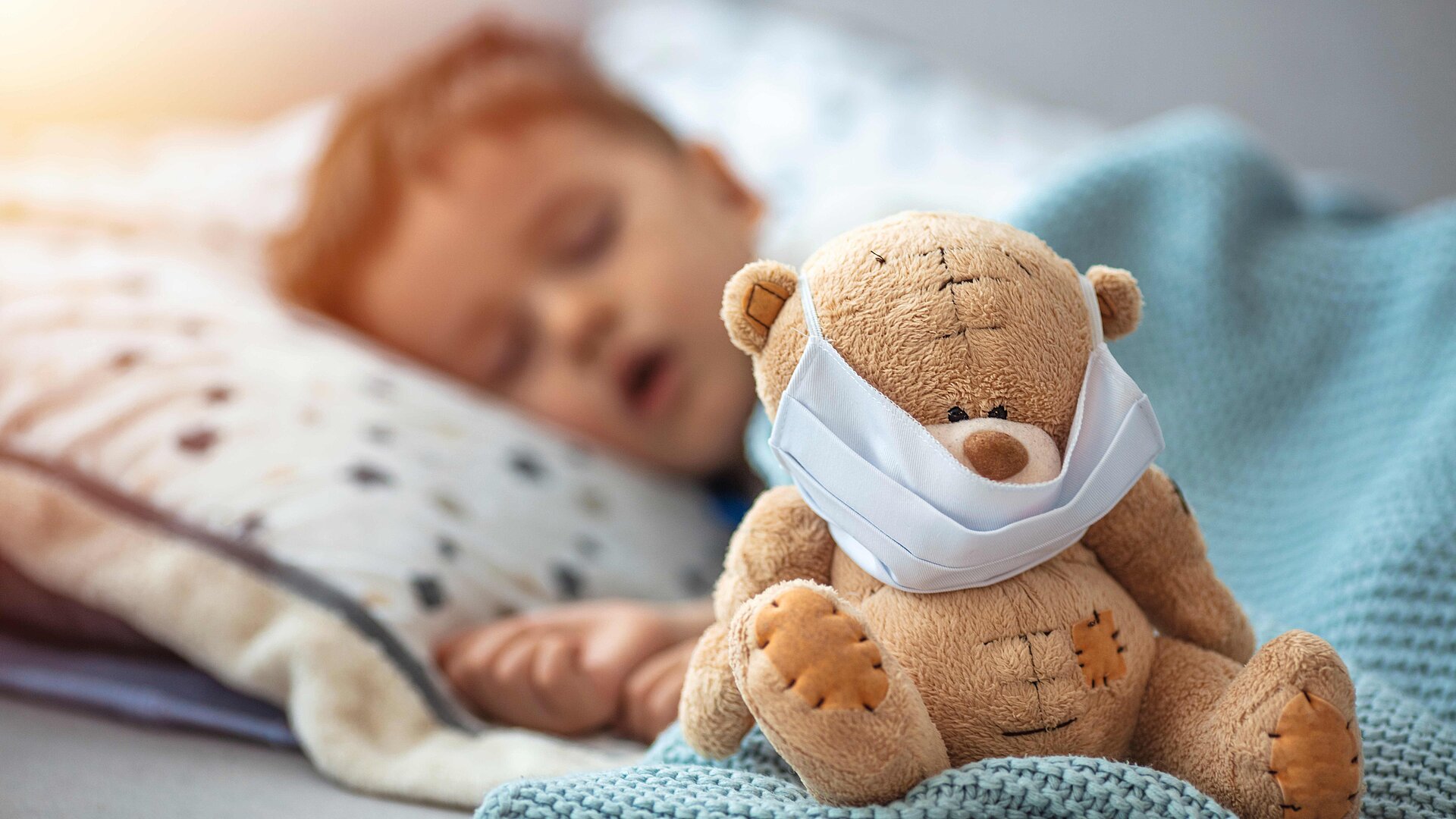 Schlafender Junge mit einem Teddy, der eine Maske aufhat