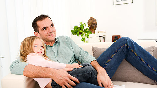 Vater und Tochter sitzen zusammen auf dem Sofa und schauen Fernseher