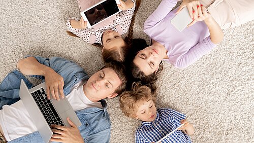 Top-Ansicht einer Familie aus vier Personen die alle an mobilen Geräten sind 